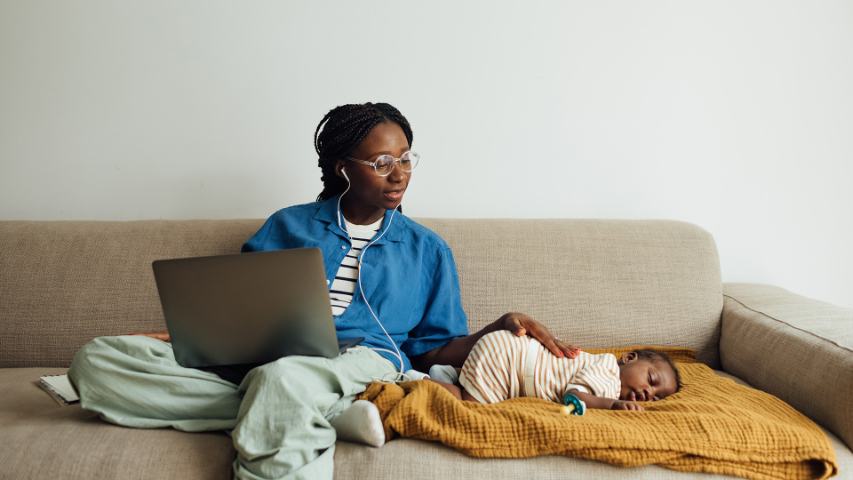 woman working on laptop with baby sleeping next to her