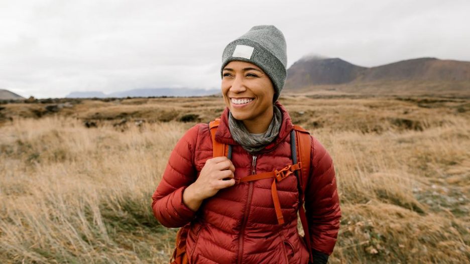 young smiling woman hiking in an orange coat with grey hat